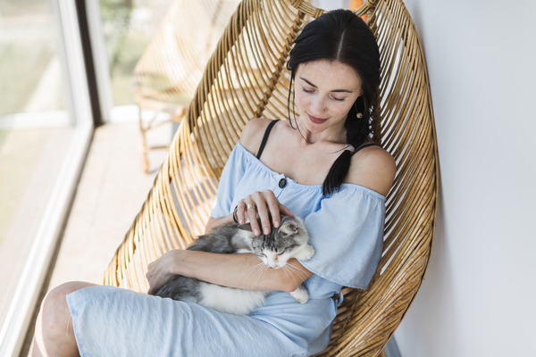 Frau mit Katze auf dem Arm sitzt im Hängesessel auf Balkon